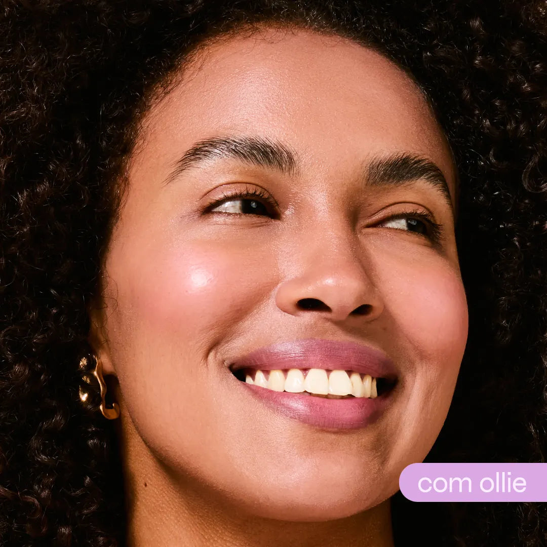 Mulher sorridente com batom bastão cor rosa-malva e blush luminoso, cabelos cacheados, pele radiante