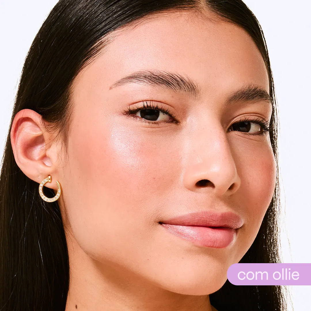 Modelo com blush rosa natural aplicado nas maçãs do rosto, pele iluminada e brinco dourado - bastão com cor Ollie