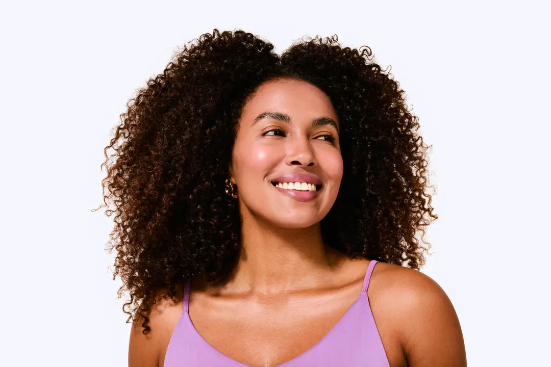 Mulher sorridente com cabelos cacheados volumosos e soltos, usando blusa lilás, resultado após usar Ollie
